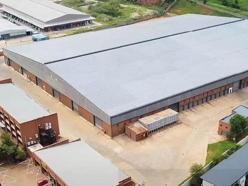 Aerial view of a large industrial warehouse complex featuring a expansive metal roof, paved yard space, and an adjacent multi-level office building.