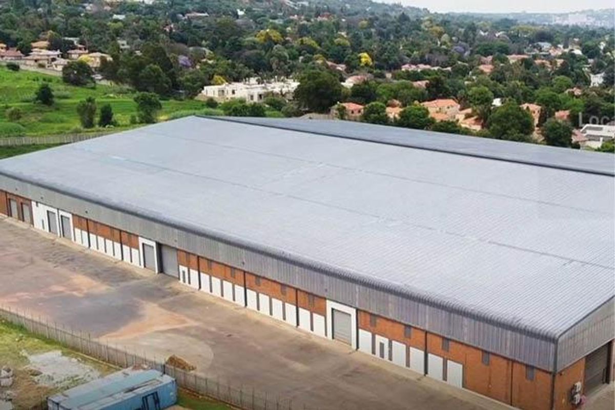 Aerial view of a large industrial warehouse facility featuring a corrugated metal roof, multiple roller shutter doors, and a brick exterior.