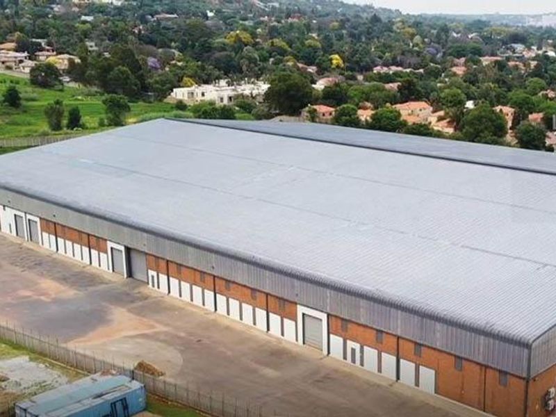 Aerial view of a large industrial warehouse facility featuring a corrugated metal roof, multiple roller shutter doors, and a brick exterior.