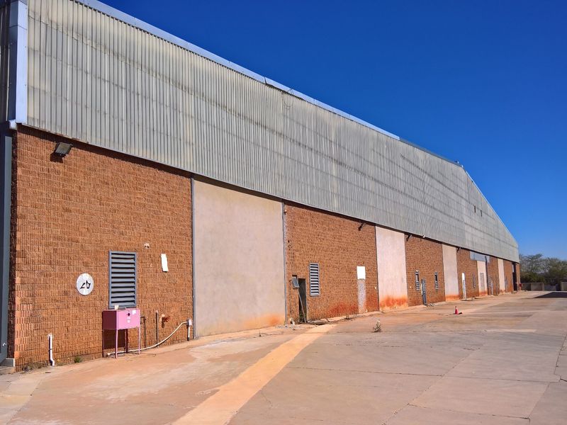 Exterior view of an industrial warehouse featuring a face brick facade, corrugated metal upper cladding, and a large concrete yard area.