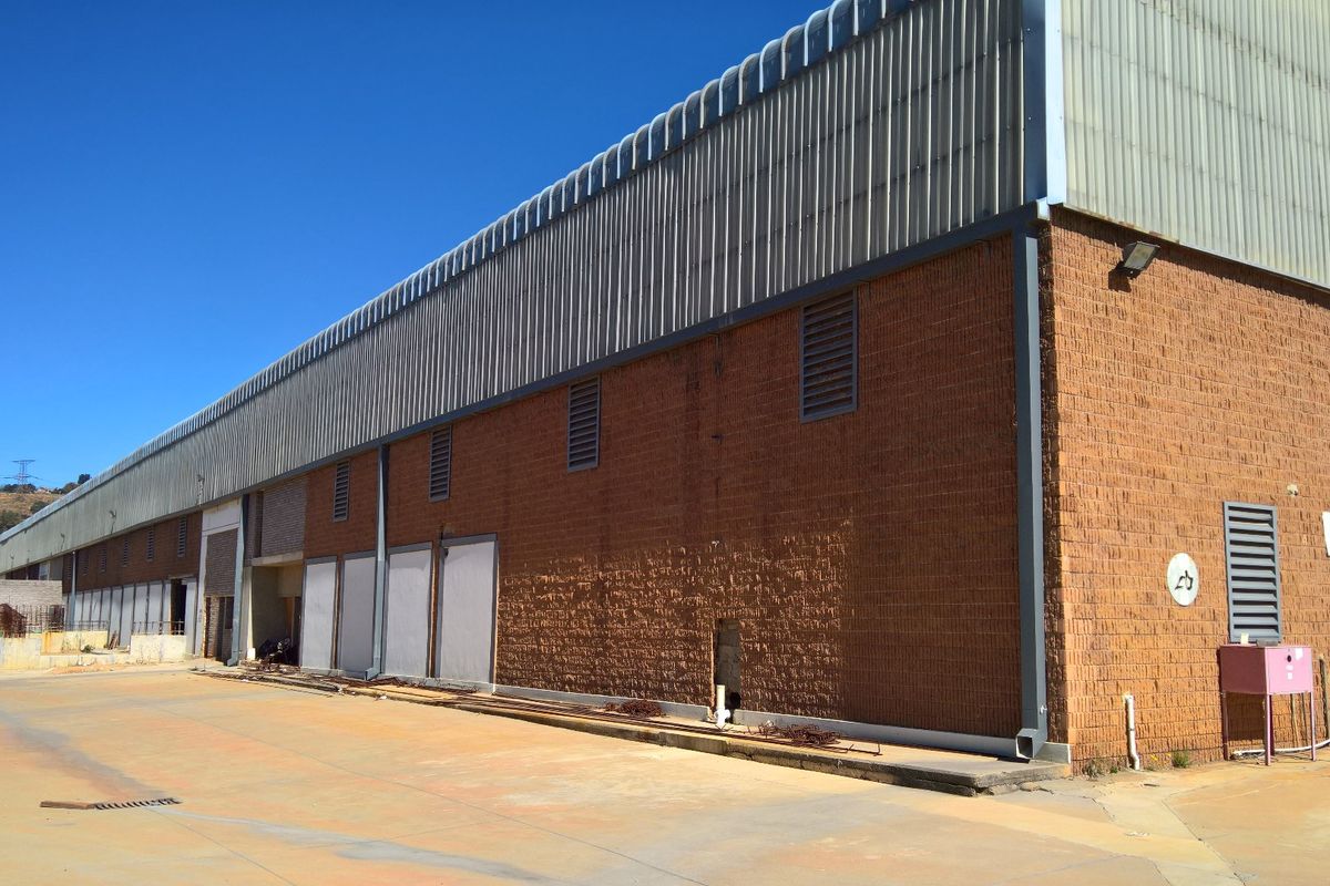 Rear exterior view of a large industrial warehouse featuring brick construction, corrugated metal upper cladding, and a concrete yard area.