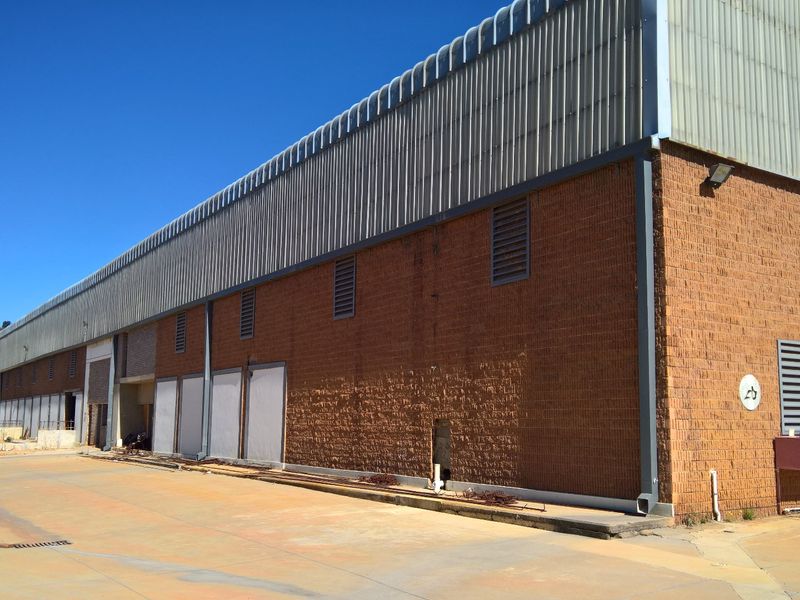 Rear exterior view of a large industrial warehouse featuring brick construction, corrugated metal upper cladding, and a concrete yard area.