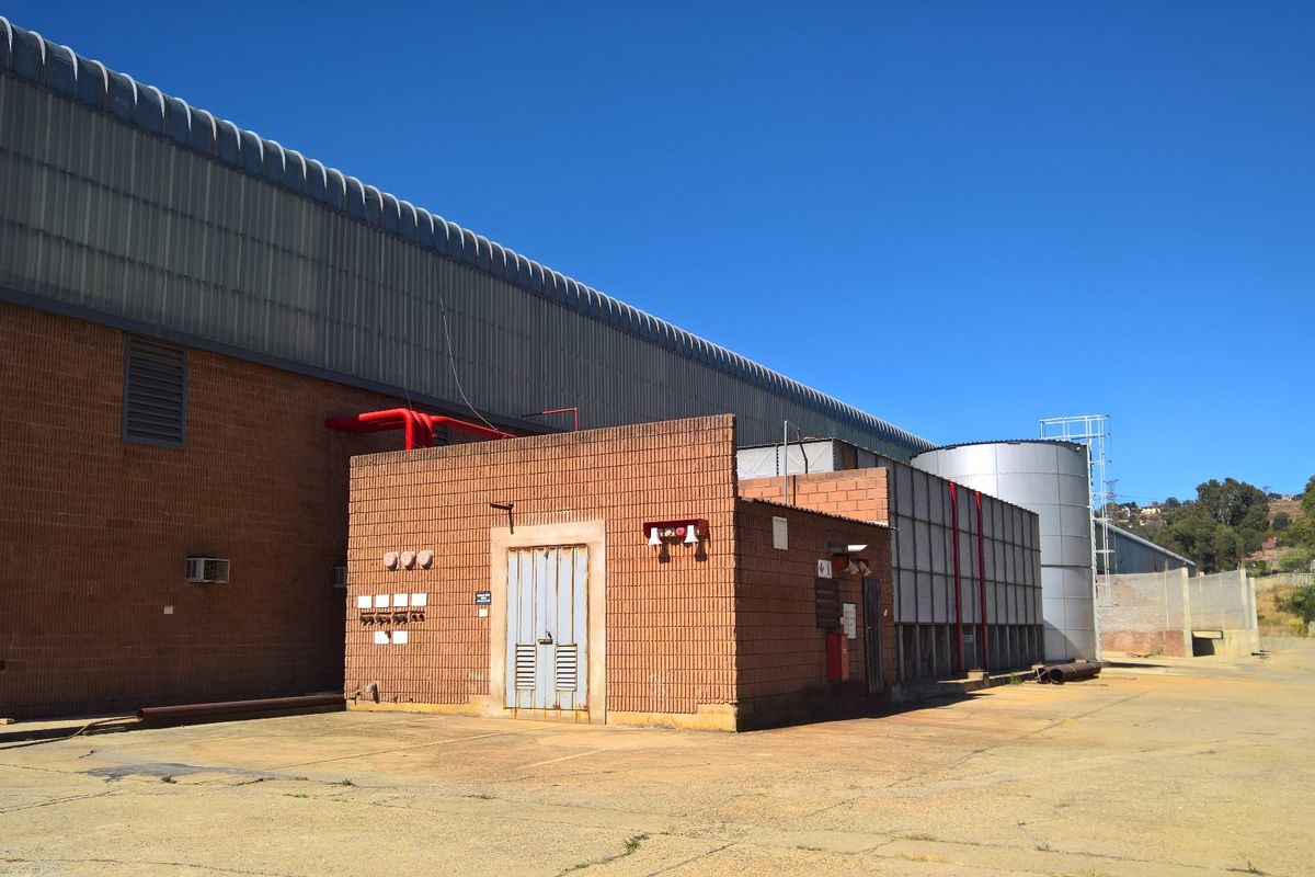 Rear exterior view of an industrial facility featuring brick construction, metal roofing, fire suppression systems, and a large water storage tank on a concrete yard.