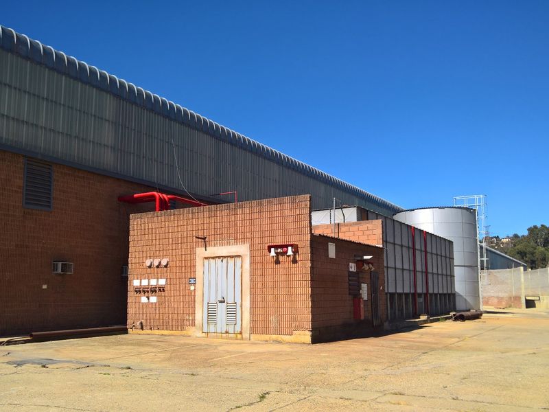 Rear exterior view of an industrial facility featuring brick construction, metal roofing, fire suppression systems, and a large water storage tank on a concrete yard.