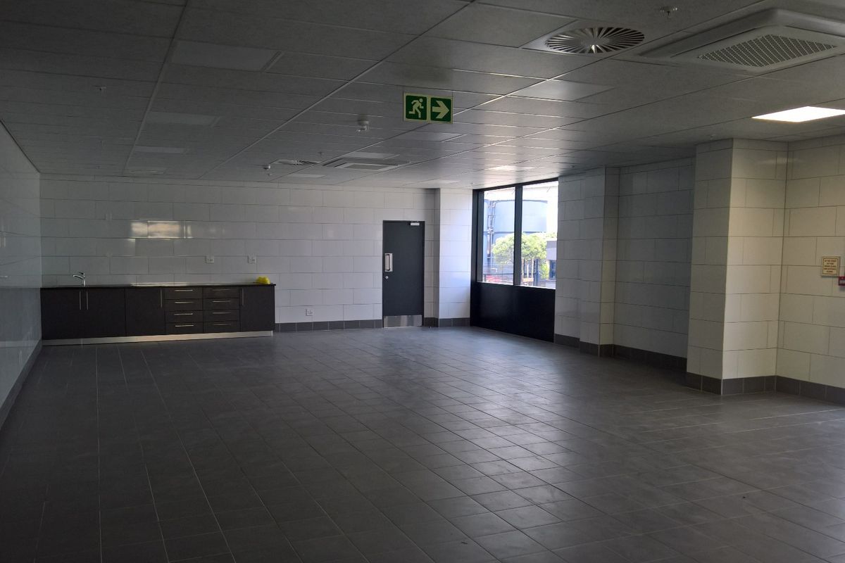 Spacious open-plan industrial office or utility area featuring tiled flooring, wall tiling, suspended ceilings, and a built-in kitchenette unit.