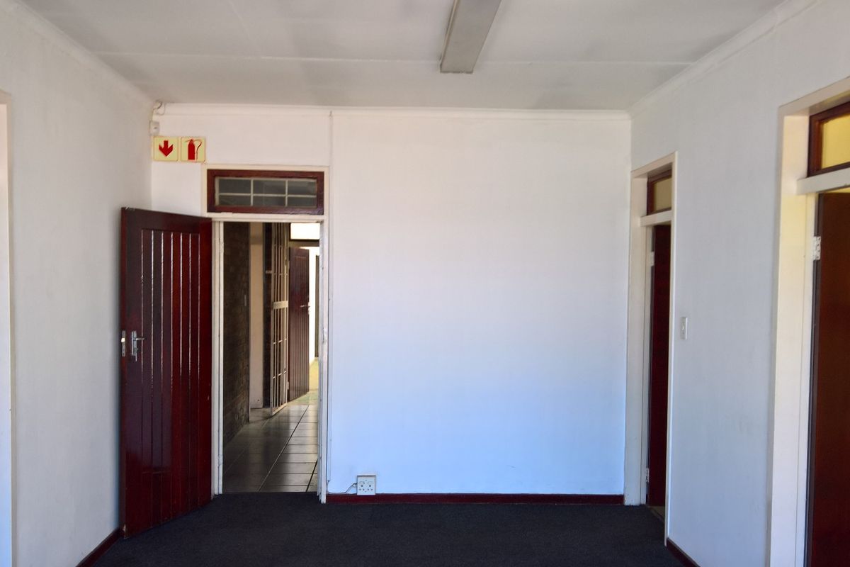 A clean, empty industrial hallway featuring white walls, dark carpeting, and multiple timber door access points with integrated fire safety signage.
