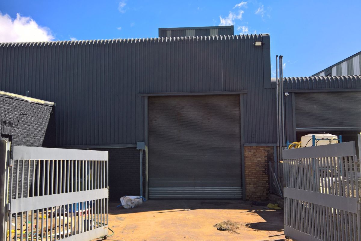 Rear industrial exterior featuring corrugated metal cladding, a large roller shutter door, and secure gated access.