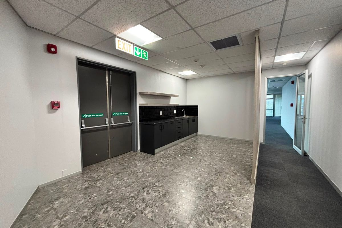 A clean, modern commercial kitchenette featuring dark cabinetry, subway tile backsplash, stainless steel sink, and integrated fire safety systems in an open office environment.