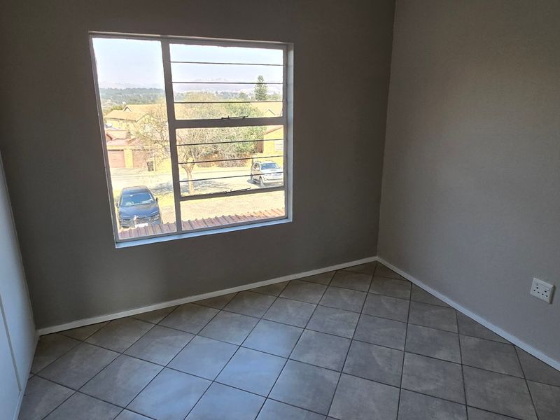A clean, empty bedroom featuring neutral grey walls, tiled flooring, and a built-in wardrobe with natural light from the window.