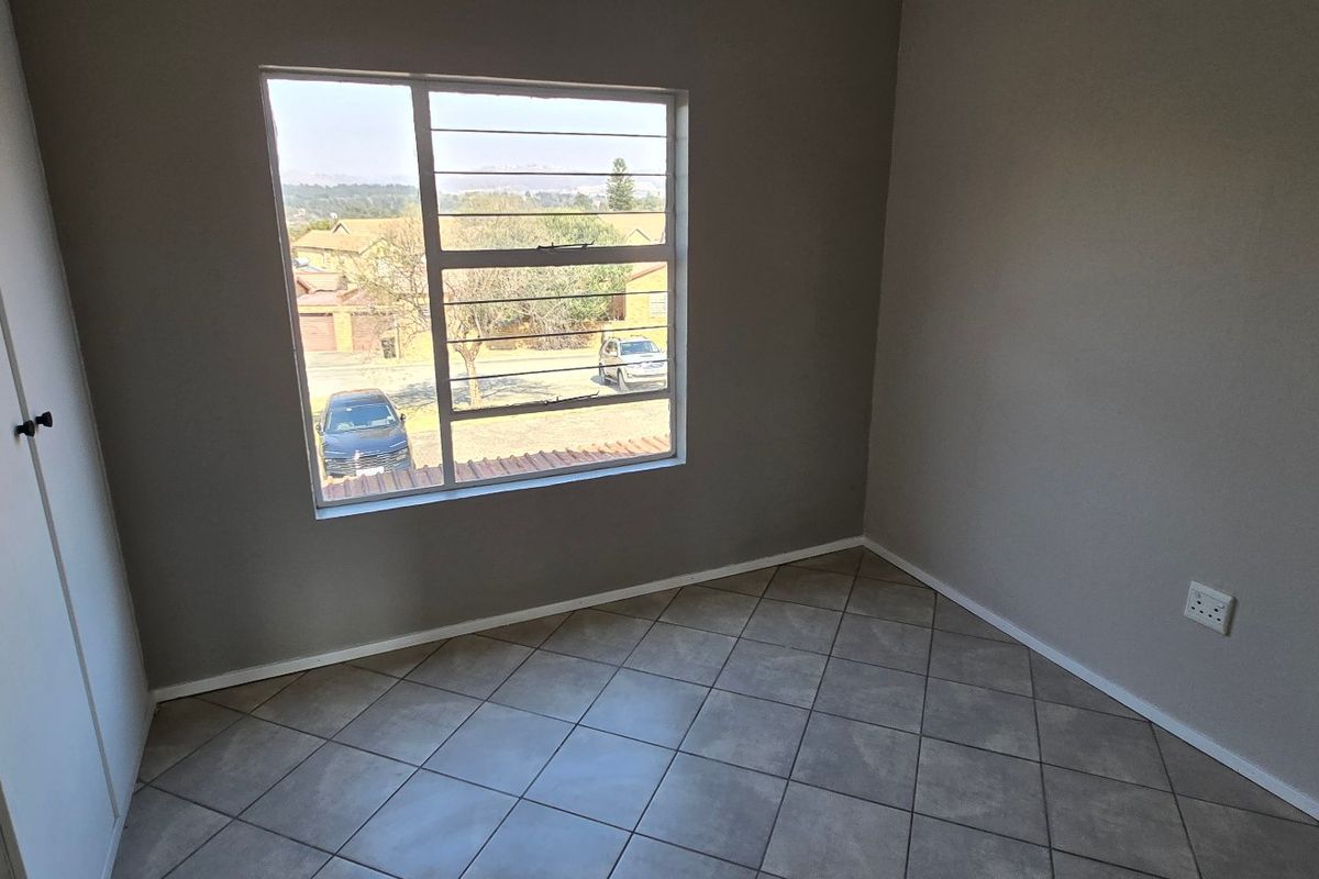A clean, empty bedroom featuring neutral grey walls, tiled flooring, and a built-in wardrobe with natural light from the window.