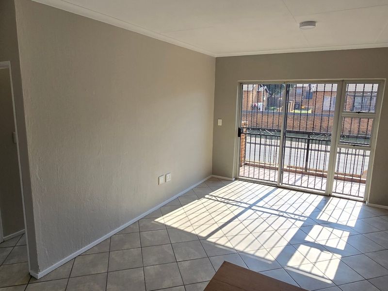 An empty living room featuring tiled floors, a built-in cupboard, and an exposed brick feature wall with access to a patio through sliding doors.