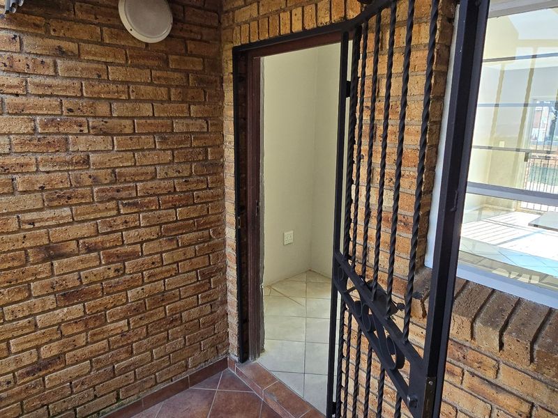 A covered patio area featuring exposed brick walls, tiled flooring, and a security gate leading into the interior of the townhouse.