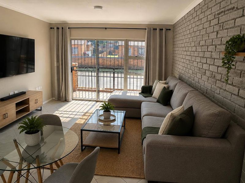 A well-maintained living room featuring an exposed brick accent wall, tiled flooring, and a sliding door leading to an outdoor area.