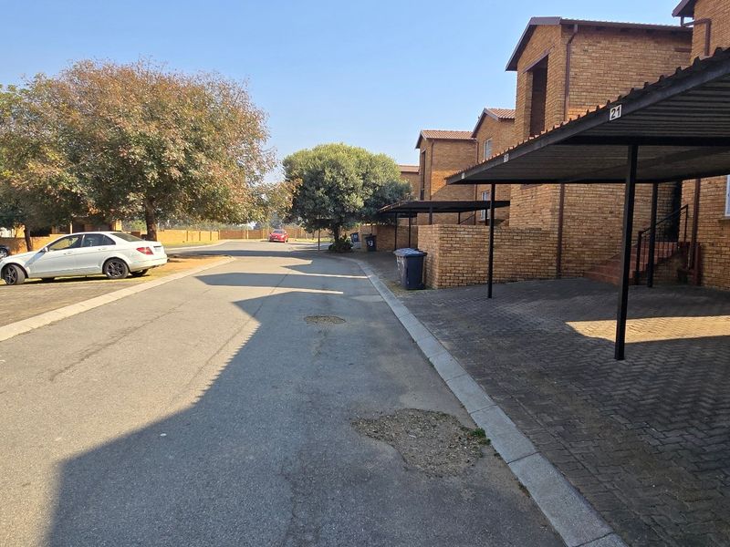Street view of a townhouse complex featuring brick facades, covered carports, and paved driveway access.