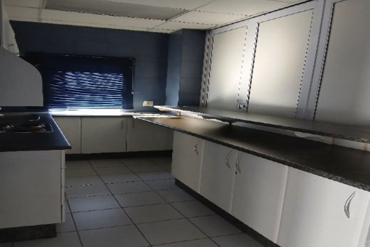 A functional industrial kitchen space featuring extensive built-in cabinetry, durable laminate countertops, and tiled flooring, offering a clean and practical layout.