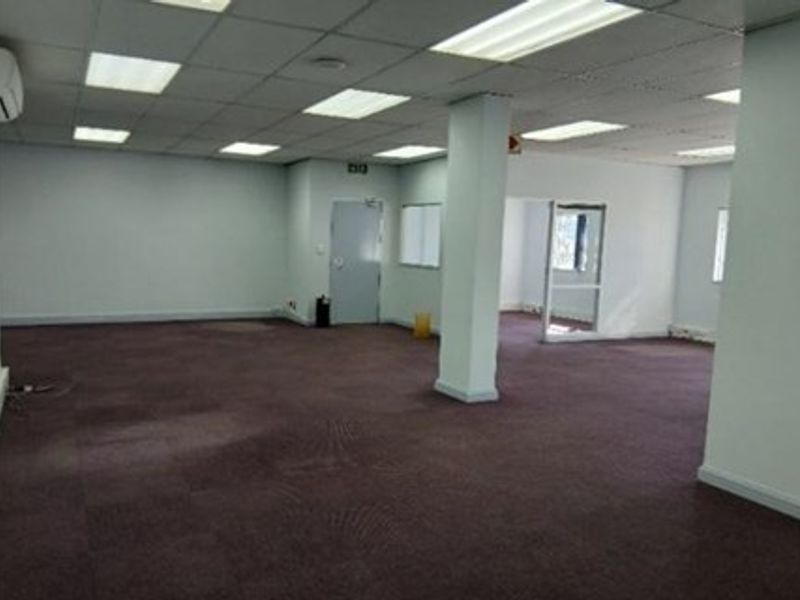 An open-plan industrial office space featuring a suspended ceiling, recessed lighting, split-system air conditioning, and carpeted flooring.