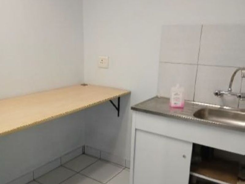 A functional laundry area featuring a stainless steel sink, tiled splashback, and a wall-mounted work surface, requiring minor repairs to the cabinetry.