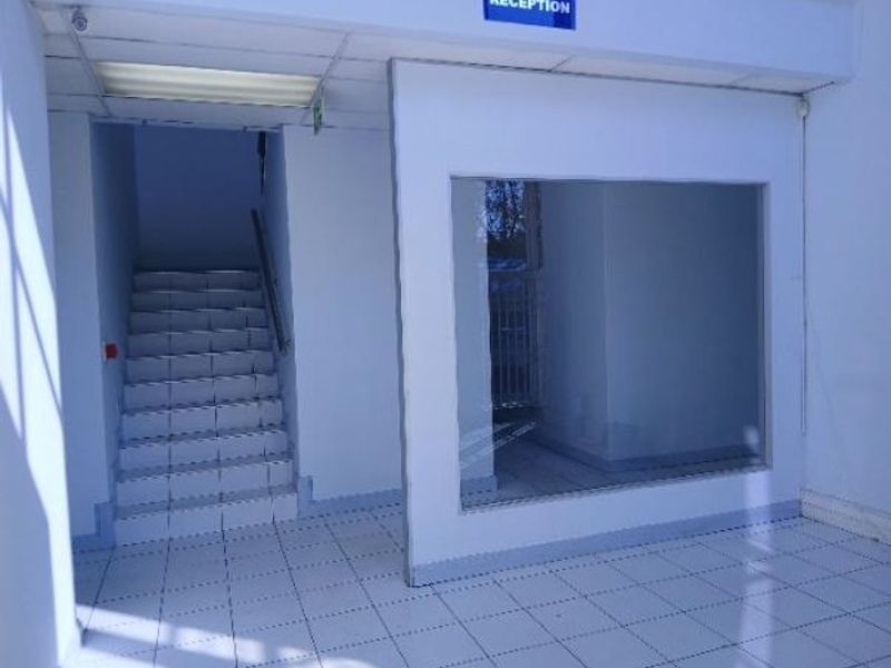 A clean, empty industrial reception area featuring tiled flooring, a staircase, and a glass partition wall.