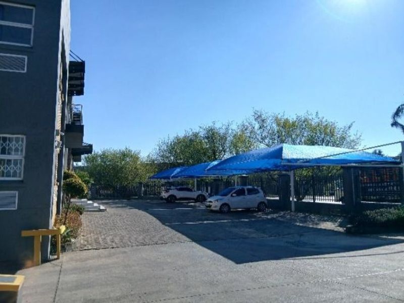 Exterior view of the industrial property featuring a paved driveway and multiple shade cloth carport structures for vehicle parking.