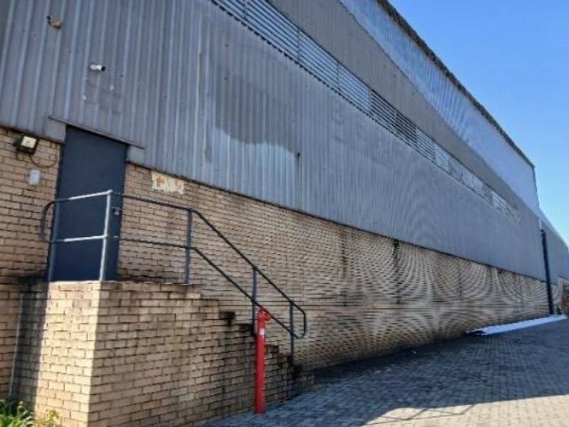 Exterior view of an industrial warehouse featuring corrugated metal cladding, face brick walls, and a metal staircase leading to a side entrance.
