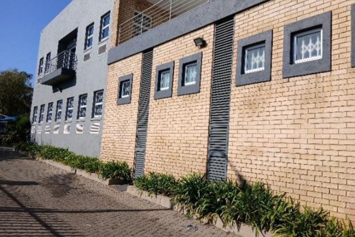 Rear exterior view of a multi-story industrial building featuring a combination of face brick and plastered finishes with balcony access and security window bars.