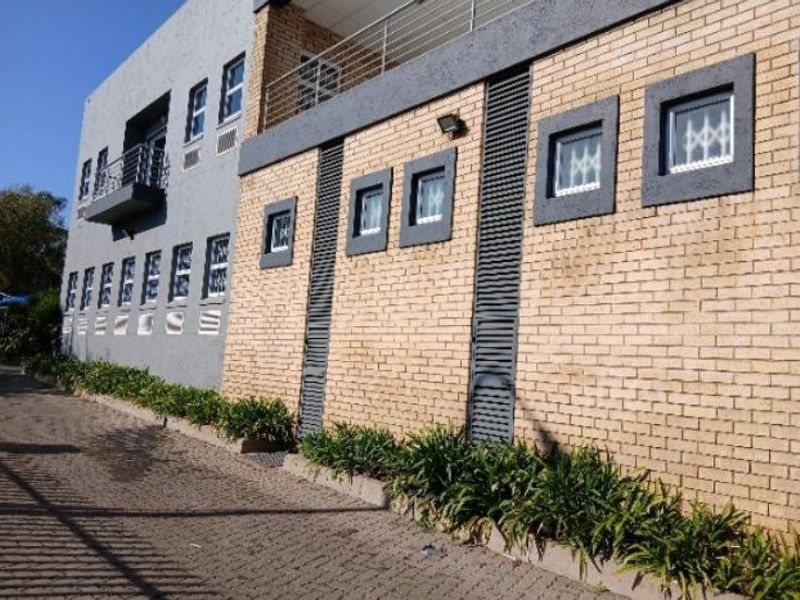 Rear exterior view of a multi-story industrial building featuring a combination of face brick and plastered finishes with balcony access and security window bars.