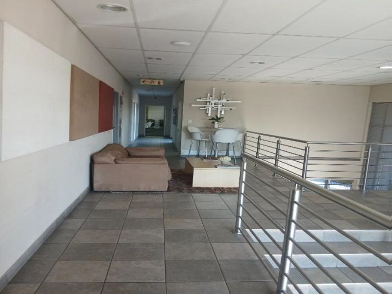 Spacious industrial hallway featuring tiled flooring, a suspended ceiling with recessed lighting, and a modern stainless steel balustrade overlooking the staircase.