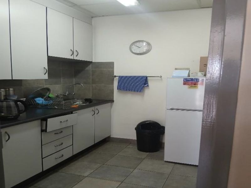 A functional industrial kitchenette featuring white cabinetry, dark laminate countertops, tiled backsplash, and tiled flooring.