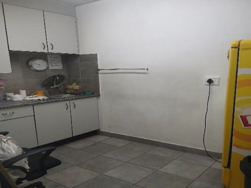 A functional kitchenette area featuring built-in cabinetry, tiled backsplash, and tiled flooring, suitable for office or industrial utility use.