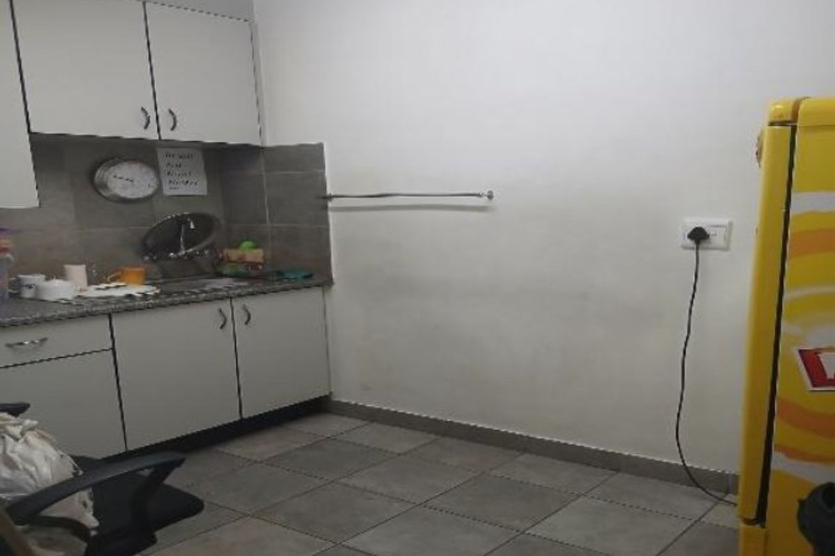 A functional kitchenette area featuring built-in cabinetry, tiled backsplash, and tiled flooring, suitable for office or industrial utility use.