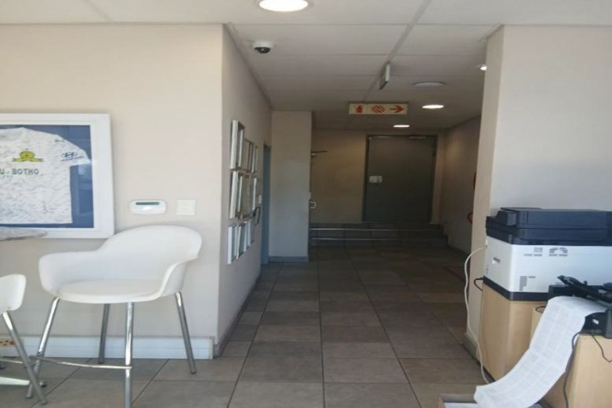 A functional industrial hallway featuring tiled flooring, recessed lighting, and a secure metal door leading to the rear exit.