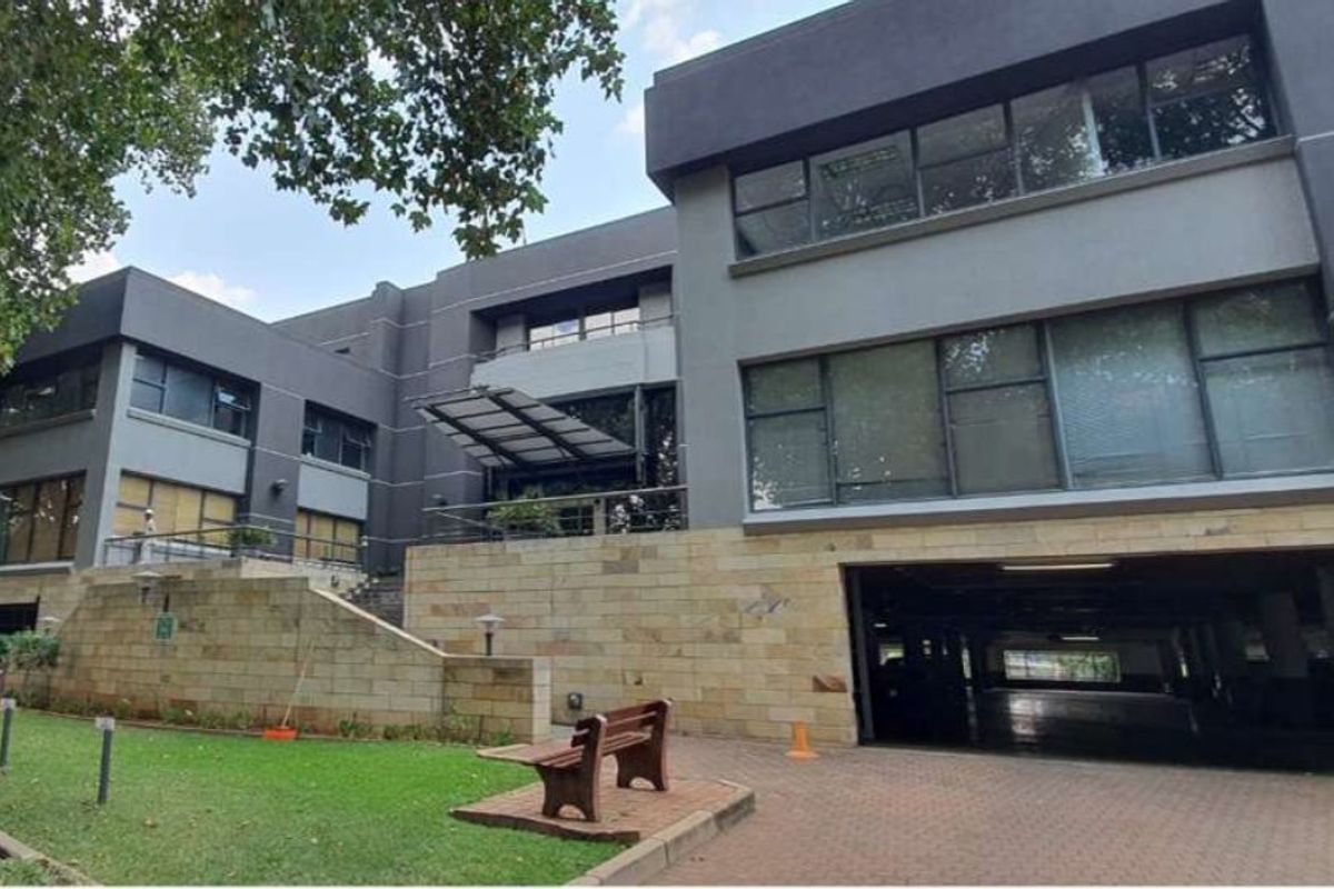 Modern commercial office building featuring stone cladding, extensive glass windows, and a convenient ground-level parking entrance.