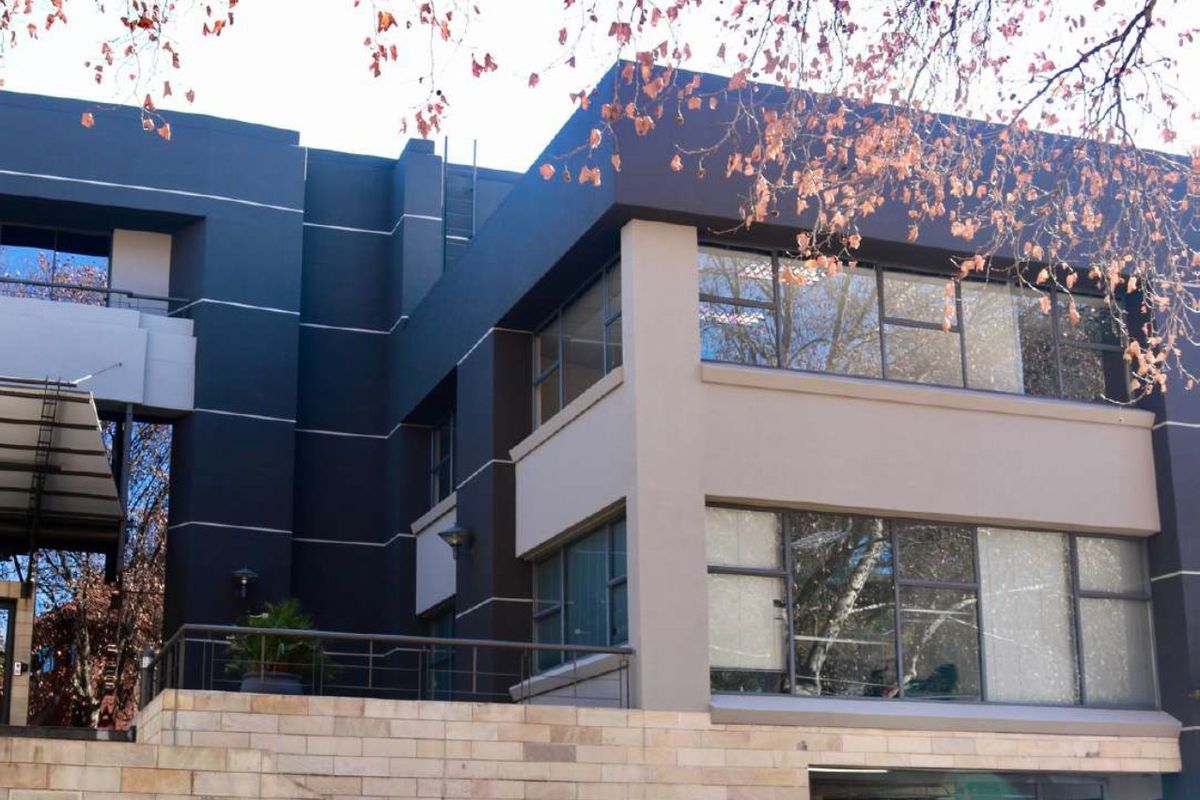 Modern commercial building facade featuring dark painted exterior walls, stone cladding accents, and large aluminium-framed windows with a balcony area.