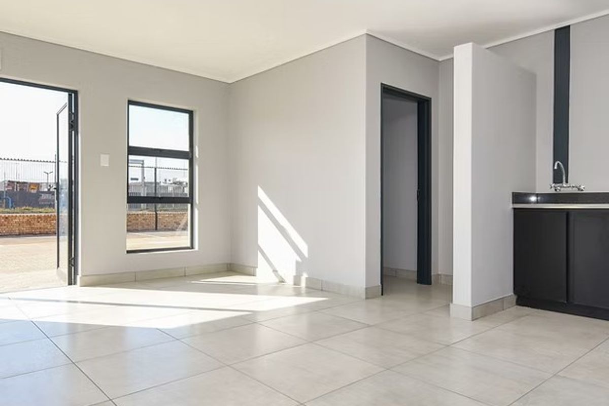 A bright, modern open-plan industrial space featuring neutral tiled flooring, a compact kitchenette with sink, and direct access to the exterior.