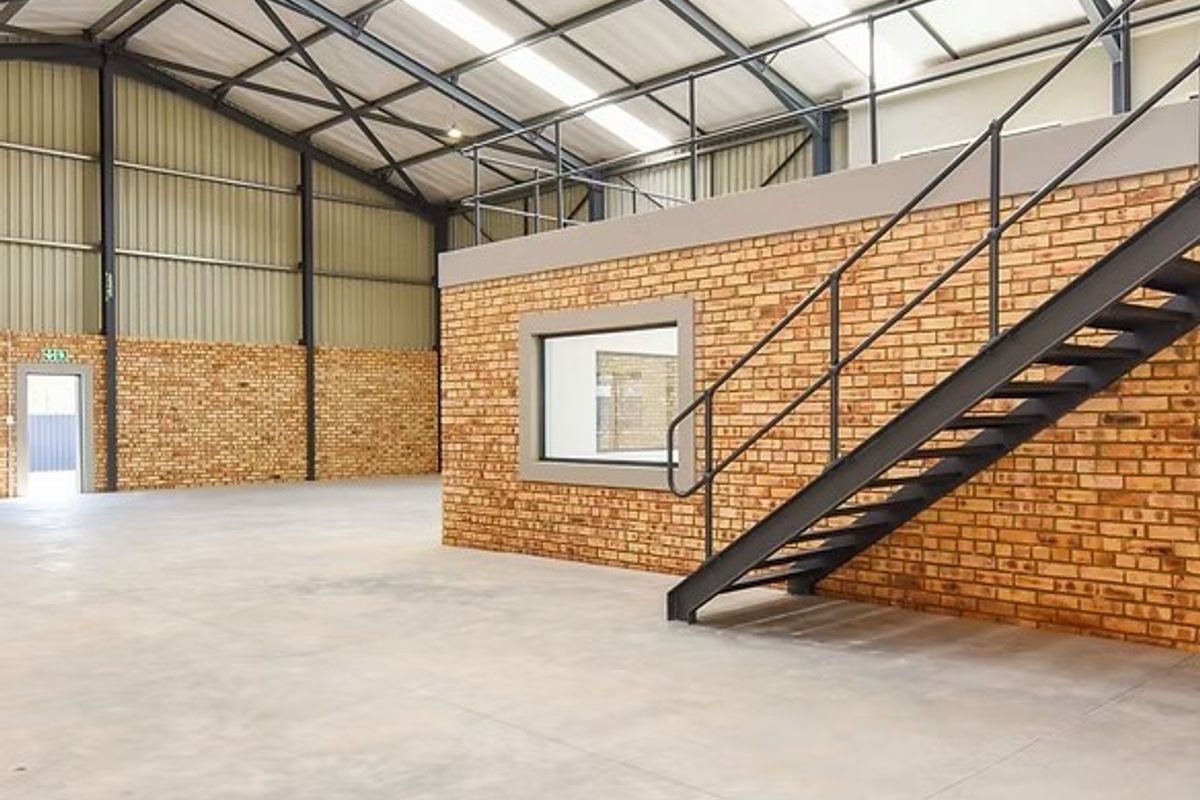 Spacious industrial warehouse unit featuring high ceilings with translucent roof panels, face brick walls, concrete flooring, and a mezzanine level with steel staircase access.