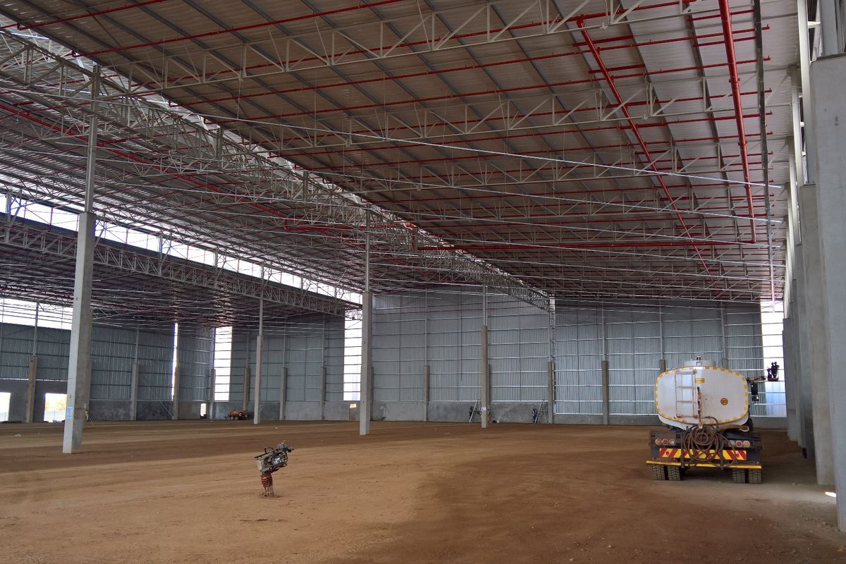 Large industrial warehouse space featuring a high-clearance steel truss roof, exposed fire sprinkler system, and concrete structural columns.