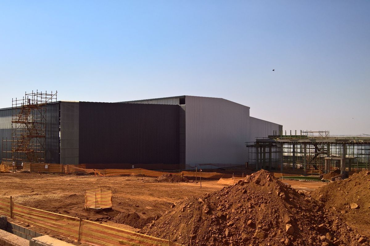 A large industrial warehouse facility currently under construction, featuring metal cladding and steel structural framing on an undeveloped site.