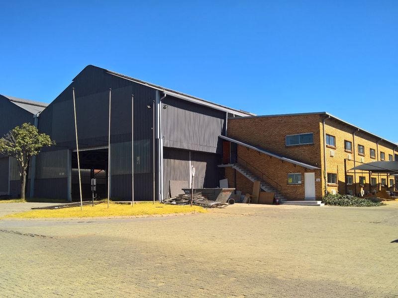 Industrial property featuring a large corrugated metal warehouse structure adjacent to a multi-level face brick office or utility building with paved exterior access.