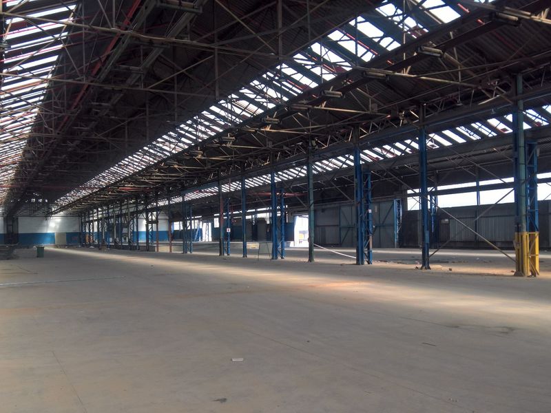 Expansive industrial warehouse space featuring high ceilings with exposed steel trusses, integrated skylights, and durable concrete flooring, suitable for various commercial or industrial operations.