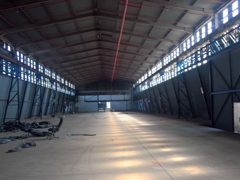 Spacious industrial warehouse featuring high ceilings, exposed steel truss framework, concrete flooring, and ample natural light from clerestory windows.