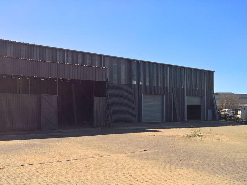 Industrial warehouse facility featuring corrugated metal cladding, multiple roller shutter doors, and a large paved yard area suitable for logistics or storage operations.