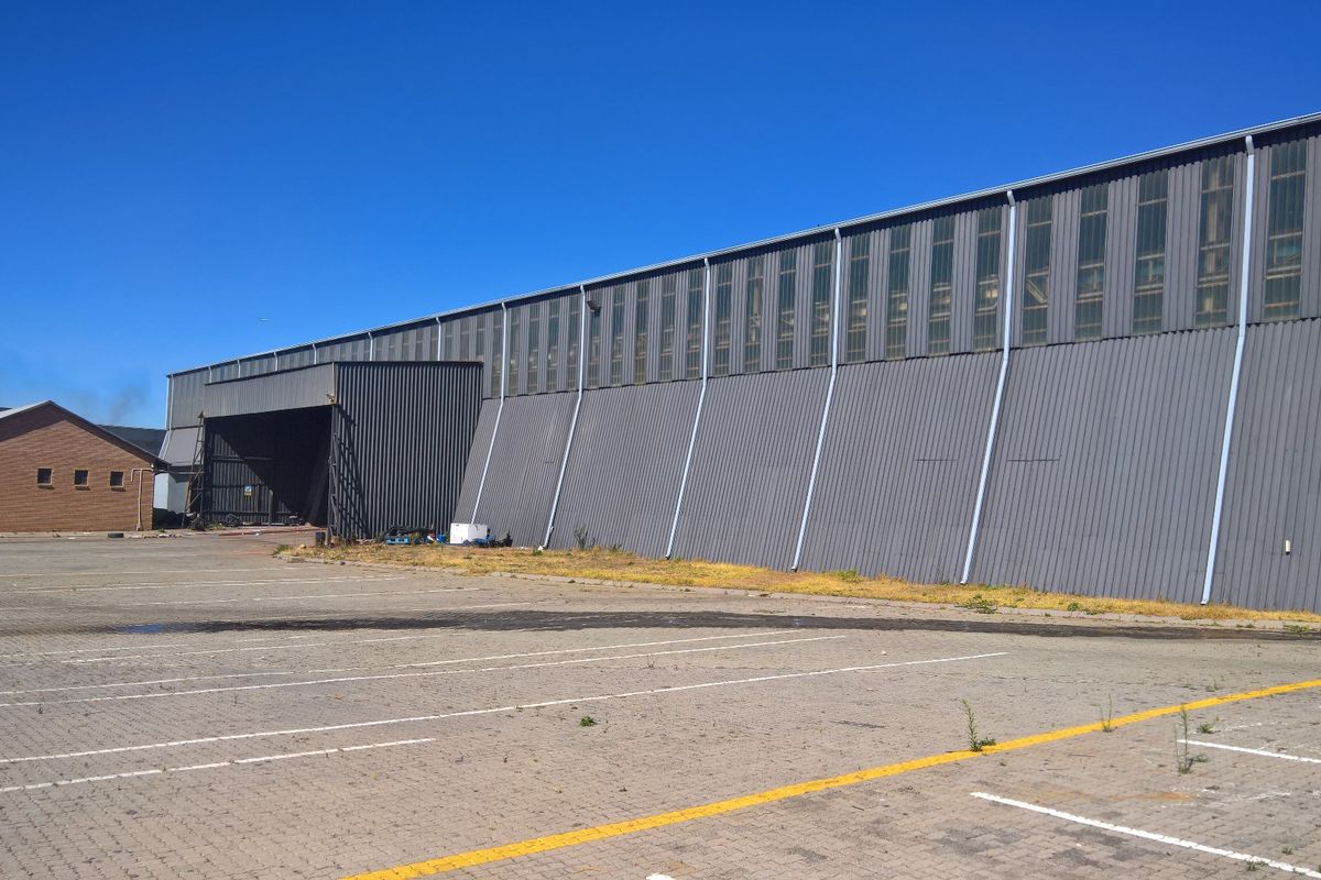 Large industrial warehouse facility featuring corrugated metal cladding, clerestory windows, and an expansive paved parking area.
