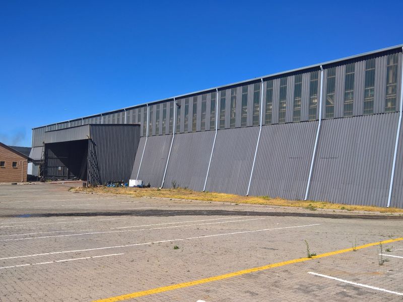 Large industrial warehouse facility featuring corrugated metal cladding, clerestory windows, and an expansive paved parking area.