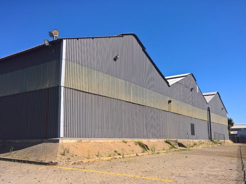 Rear view of an industrial warehouse featuring corrugated metal cladding, a pitched roof design, and an expansive paved yard area.