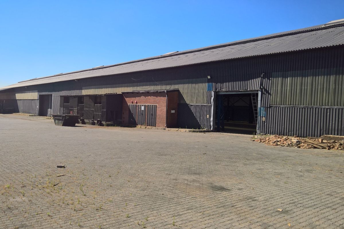 Large industrial warehouse facility featuring extensive corrugated metal cladding, multiple access points, and a spacious paved yard area suitable for logistics or storage.