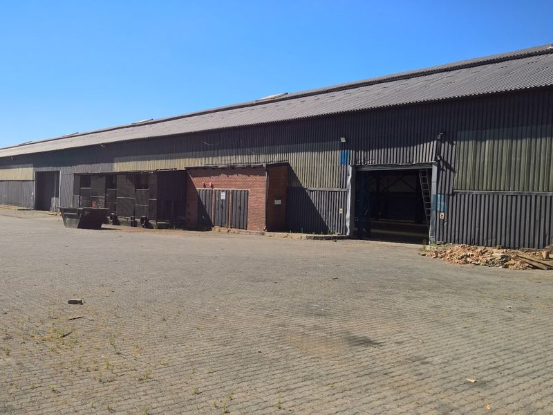 Large industrial warehouse facility featuring extensive corrugated metal cladding, multiple access points, and a spacious paved yard area suitable for logistics or storage.
