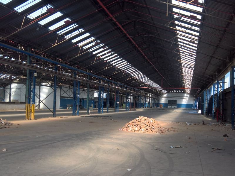 Expansive industrial warehouse space featuring a high steel portal frame, concrete flooring, and extensive skylights providing natural illumination throughout the open floor plan.