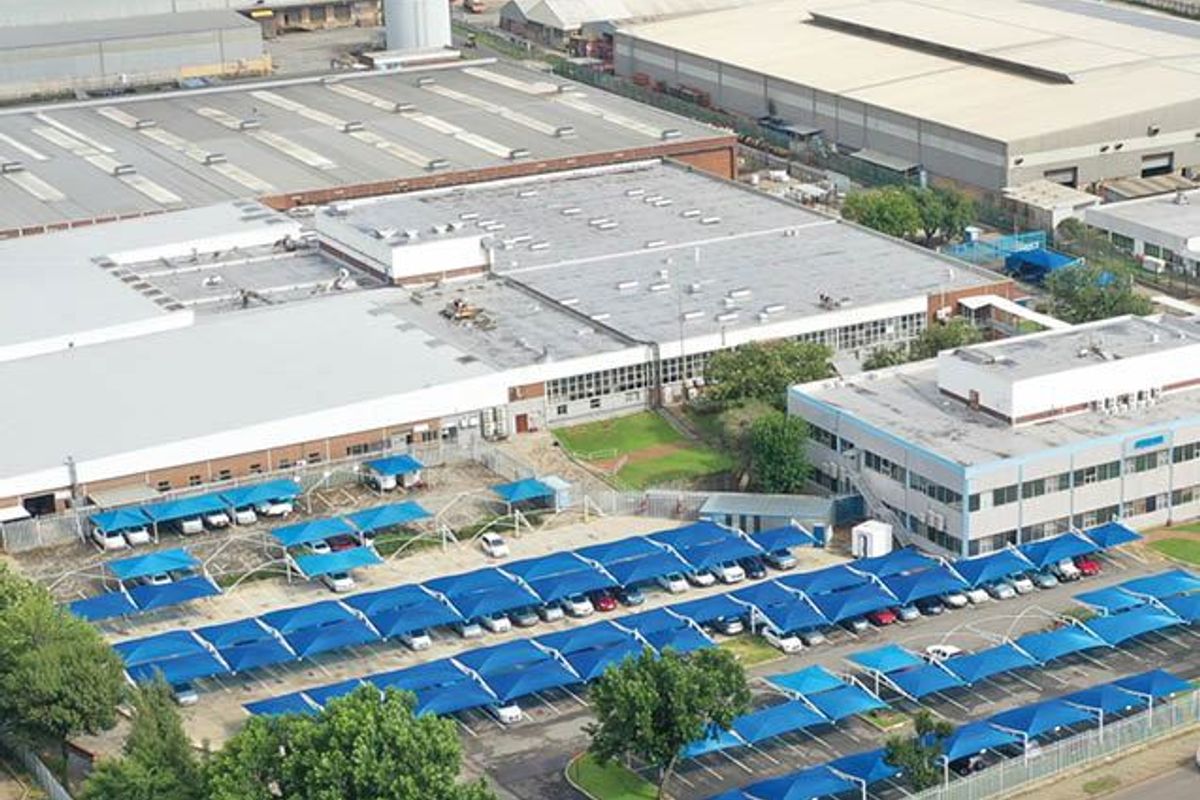 Aerial view of an industrial property featuring a large warehouse facility, office block, and extensive covered parking area.