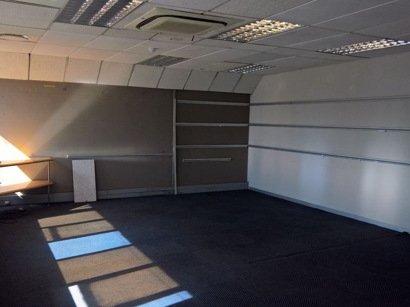 An empty industrial office space featuring suspended ceilings, recessed lighting, air conditioning, and wall-mounted shelving tracks, suitable for various commercial or administrative uses.