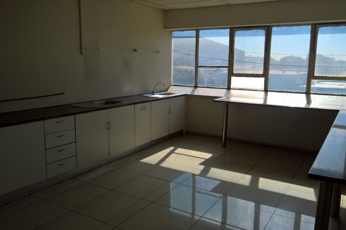 A functional industrial kitchen space featuring built-in cabinetry, stainless steel sinks, tiled flooring, and large windows providing ample natural light.